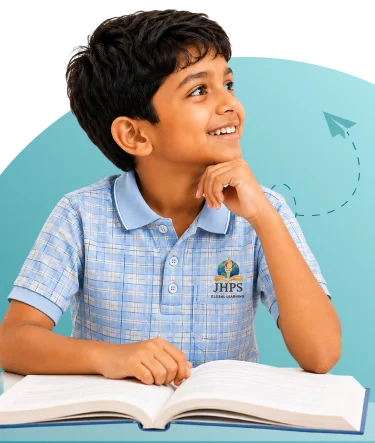 A smiling JHPS student resting his chin on his hand over an open book